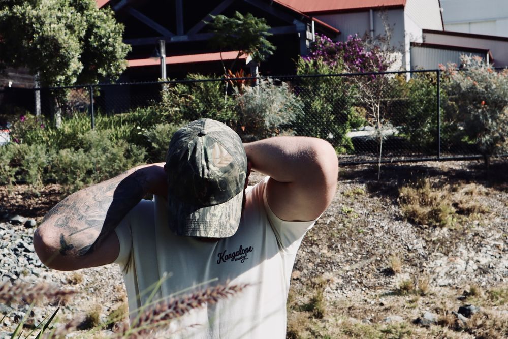 Bush Camo hat worn with arms raised at the creek on the farm