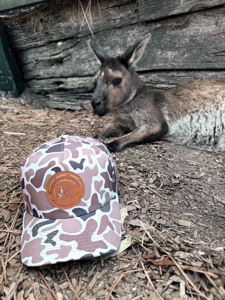 Bush Camo hat on a fence rail with a wallaby lying in the grass behind