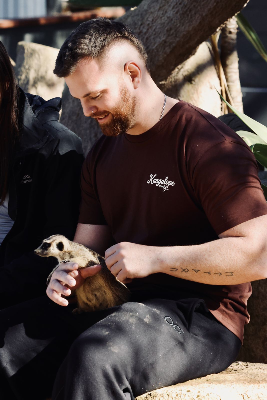 Front of the Chestnut Brown tee worn at a wildlife park, holding a meerkat