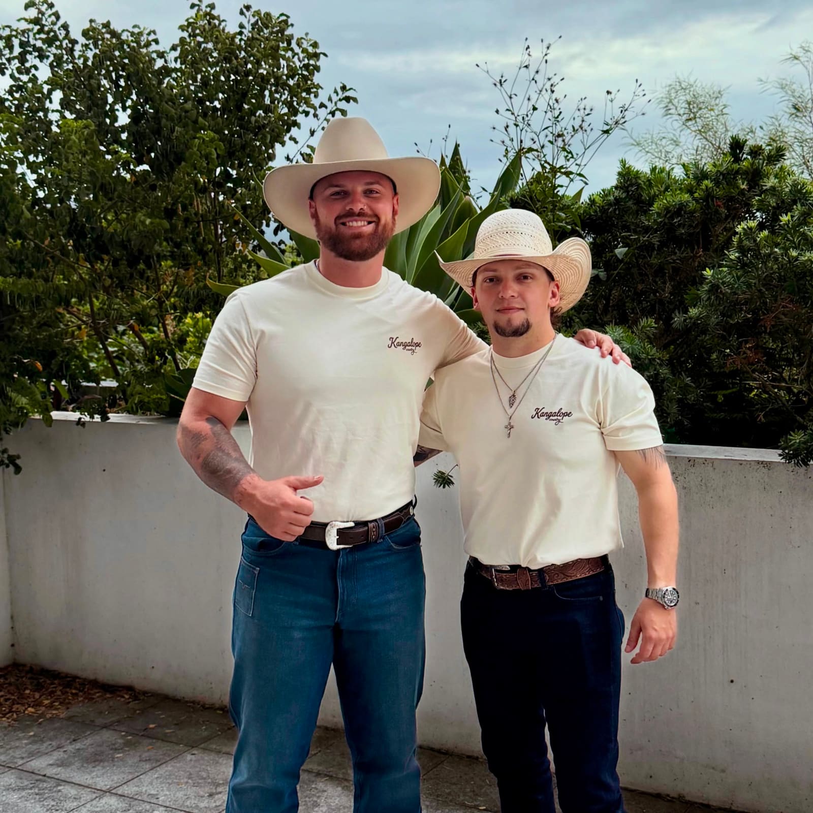 The two founders standing together in Ecru Kangalope Country tees and cowboy hats - one Aussie, one Texan